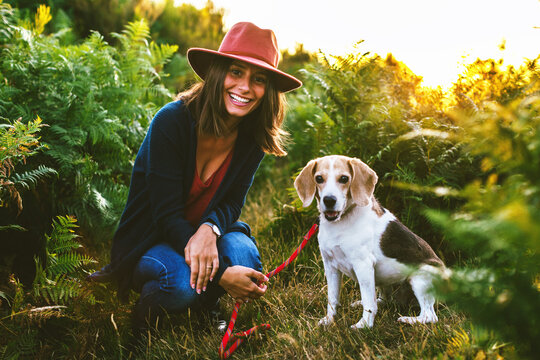 Portrait of a hipster woman with her beagle dog standing on the forest at sunset.