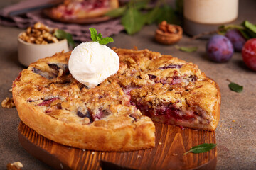 Closed pie filled with plums and walnuts. Sweet homemade dessert served with vanilla ice cream.
