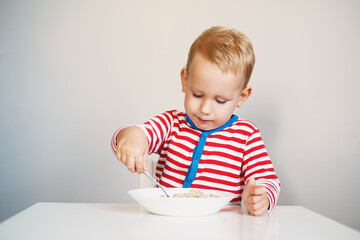  child is holding a spoon in his hands and eats porridge while sitting at the table.