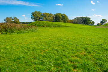 Dike in a green grassy field in sunlight under a blue sky in autumn, Almere, Flevoland, The Netherlands, September 24, 2020
