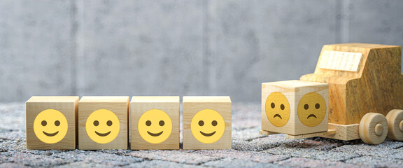 cubes with happy emoticons and a forklift carrying another one with a sad smiley on concrete background © fotogestoeber