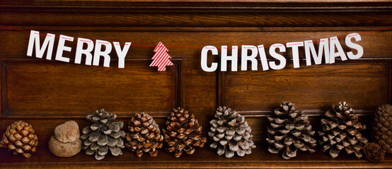 Paper garland saying Merry Cjristmas and pine cones on fireplace top