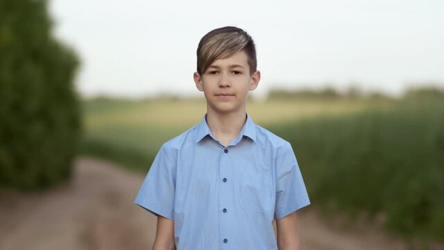 portrait of a happy boy standing in nature near the field and looking at the camera
