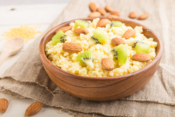 Millet porridge with kiwi and almonds in wooden bowl on a white wooden background. Side view, selective focus