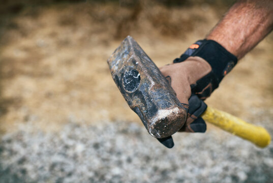 Holding a small sledge hammer with gloves on.