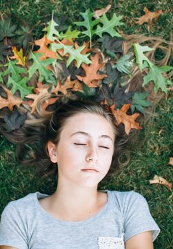 Teenage girl laying in the grass with her long hair decorated with fallen leaves