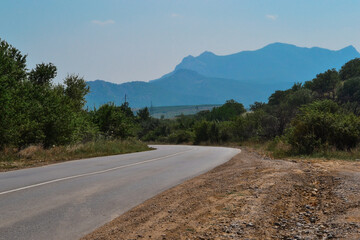 Asphalt village road in the forest against the background of high beautiful sharp blue mountains. Summer Crimea, trees