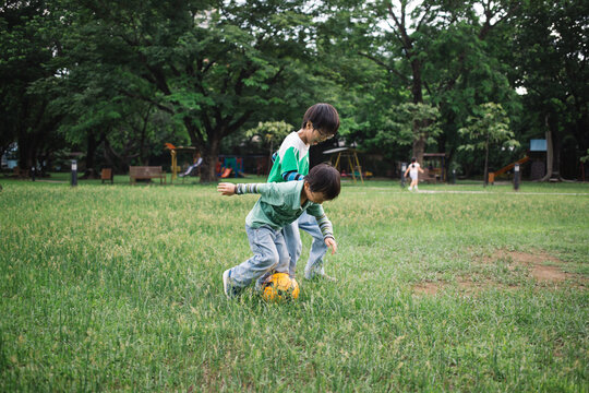 Two young brothers playing football in a park on a Sunday