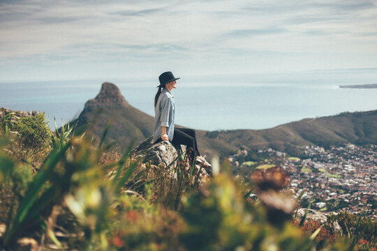 woman wearing hat sitting on mountain overlooking view
