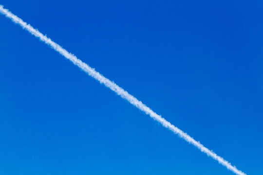 White contrail against blue sky on a sunny day looking up