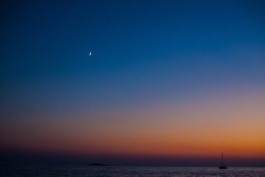 Beautiful sunset on the sea with a boat and a moon in the background