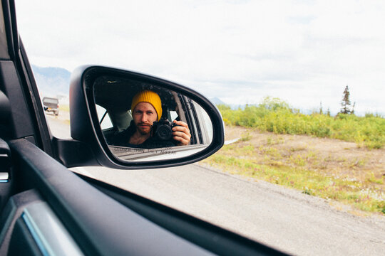 A Young Man Wearing A Yellow Beanie Takes A Selfie With His Camera In The Passenger Side Car Door Mirror
