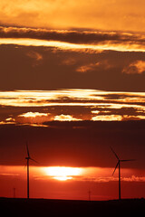 Two wind turbines standing in front of a cloudy, distant sunset