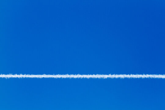 White contrail against blue sky on a sunny day looking up