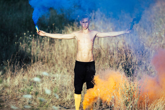 young boy in yellow stockings holding colorful smoke bombs in nature