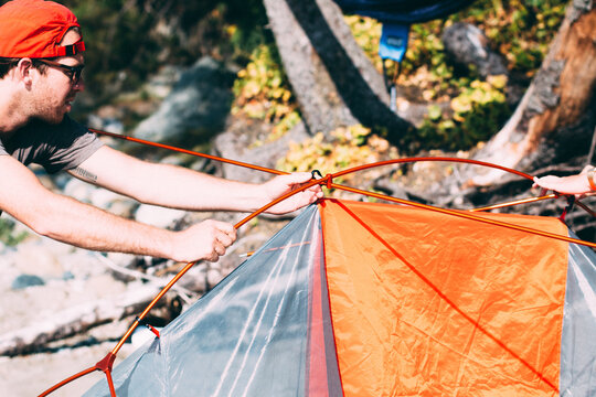 A Young Man Wearing A Red Cap Sets Up An Orange Tent On The Beach