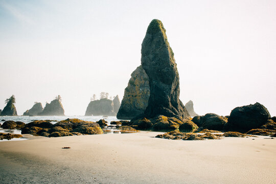 A Solitary Rock Spire Eroded By The Ocean Stands Tall On A Sandy Beach