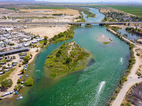 a stunning aerial shot of the deep green waters of the Colorado River with lush green trees, boats on the water and buildings with blue sky at Queshan Park in Blythe California