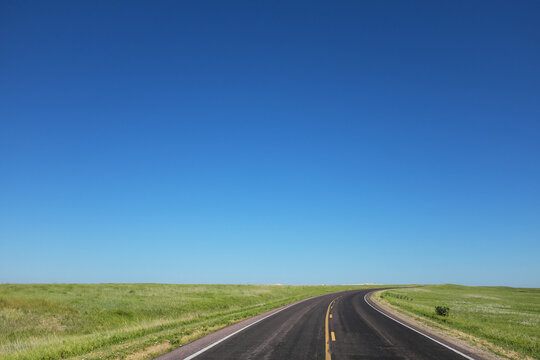 Two lane highway across the Great Plains of North America under a cloudless sky