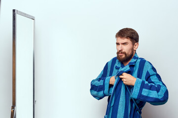 a man in a blue robe examines himself in a mirror in a bright room cropped view