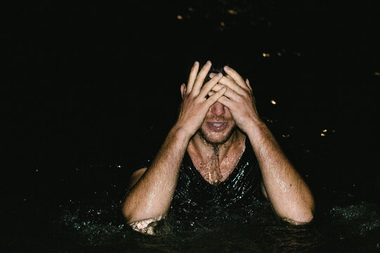 Man Standing In Chest Deep Water Holding Hands Over Face
