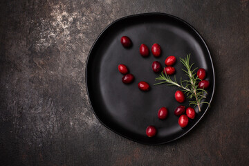 Top View of Cranberries with a Sprig of Rosemary on a Black Plate against a Black Textured Background