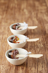Various chocolate pops decorated with ribbon and sprinkles on a brown wood background.