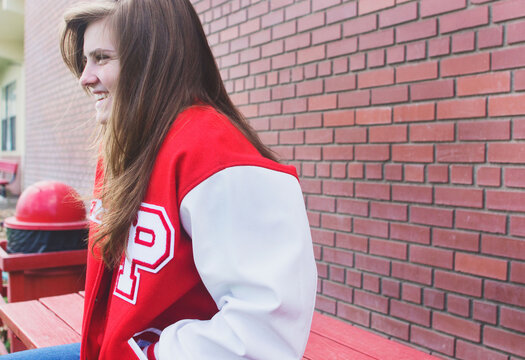 Teenage girl wearing letterman jacket sits on table