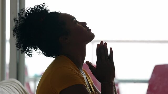 Young black woman praying raising face up to the sky