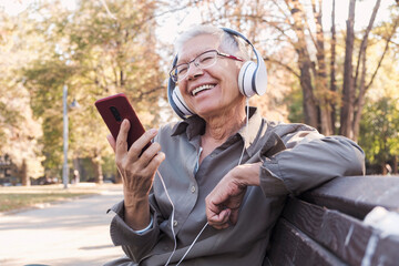 Senior old woman listening to her favourite music through big headphones,