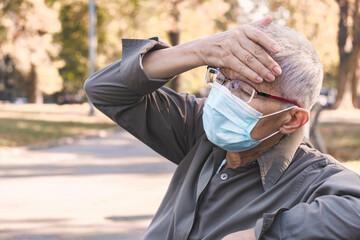 Frustrated senior woman having a headache with a mask on