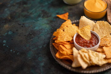 The plate with tortilla nachos and souses are in the corner of photo. Dark background. Fast food concept. Tasty tortilla chips. Unhealthy food.