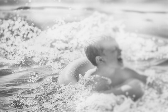black and white atmosphere,a blond boy with a swimming ring enjoying in the sea