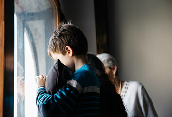Boy holding his pillow by the window sadly waving bye to someone