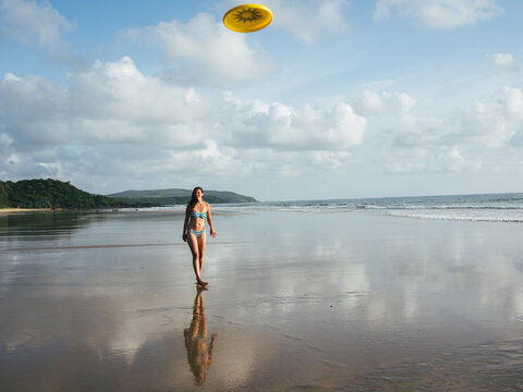Girl in swimsuit throwing frisbee on the beach