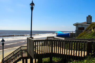a wooden staircase to the beach with light posts, vast ocean water, blue sky and lush green...