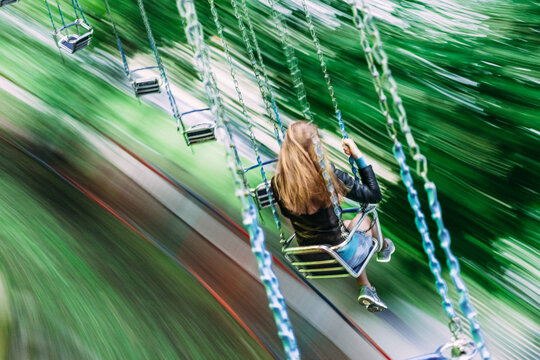 Young woman riding on a swing carousel in amusement park smiling