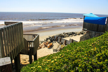 a wooden staircase to the beach with light posts, vast ocean water, blue sky and lush green...