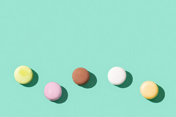 Pattern from different cake macaroons on bright blue green color background, multi colored french biscuit macarons.
