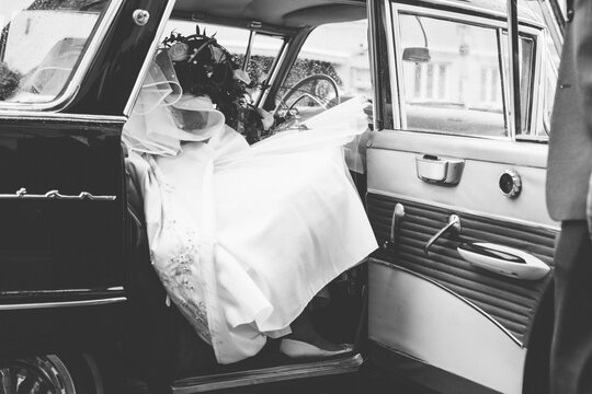 bride in white wedding dress getting out of an oldtimer car in black and white