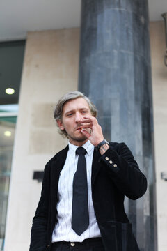 Stylish businessman smoking cigarette outdoors