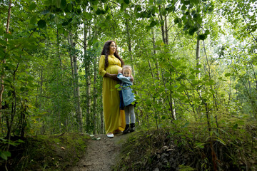 Pregnant woman in yellow dress with her daughter in nature