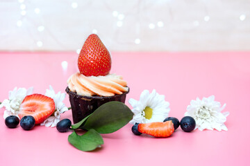 birthday cupcake decorated with large strawberries and flowers on a pink background