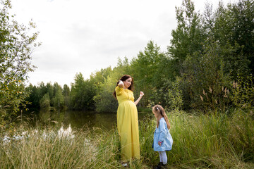 Pregnant woman in yellow dress with her daughter in nature