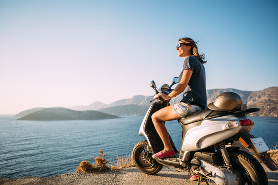 woman on a moped overlooking the sea at sunset