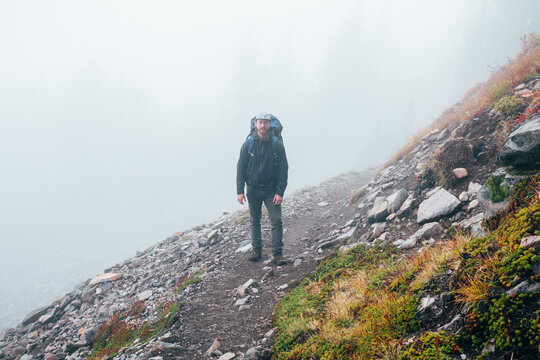 Young Male Backpacker Standing On Dirt Trail Along Mountainside