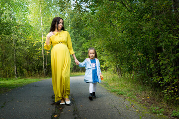 Fototapeta premium Pregnant woman in yellow dress with her daughter in nature
