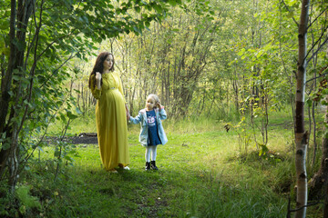 Pregnant woman in yellow dress with her daughter in nature