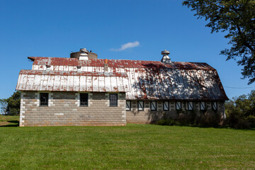 An abandoned old farm house with a tall brick silo and a big barn with rusted tin ceiling. This very old run down builsing complex is surrounded by grassland and trees. Image taken in rural Maryland.