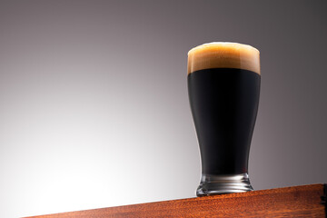 Close up photo of a Glass of dark beer on a Wooden Surface and Gradient Background
